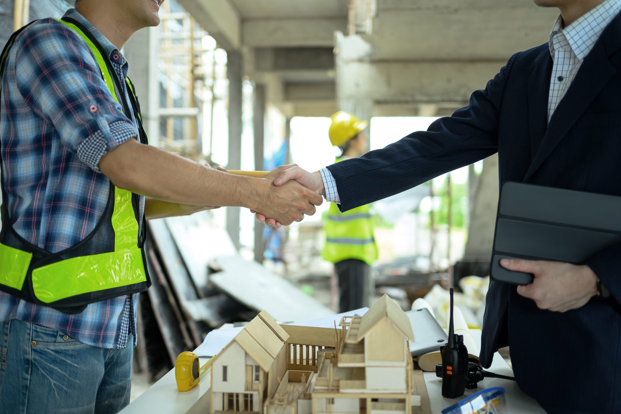 Stretta di mano tra un tecnico di cantiere e un cliente davanti a un plastico edilizio