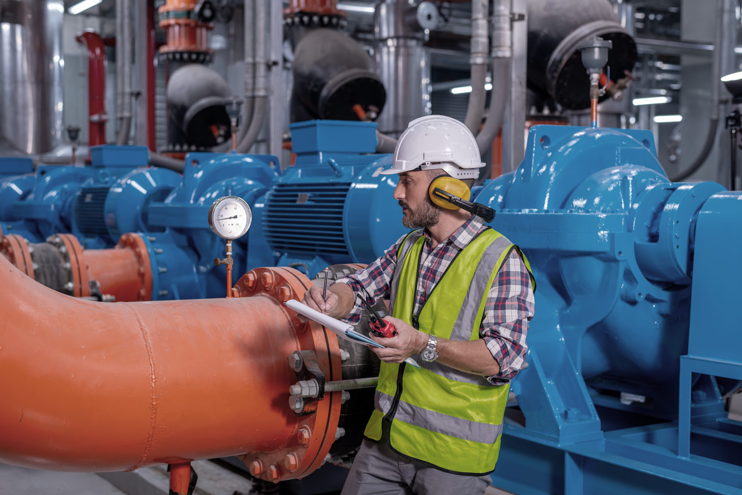 Tecnico con dispositivi di protezione che controlla un impianto industriale